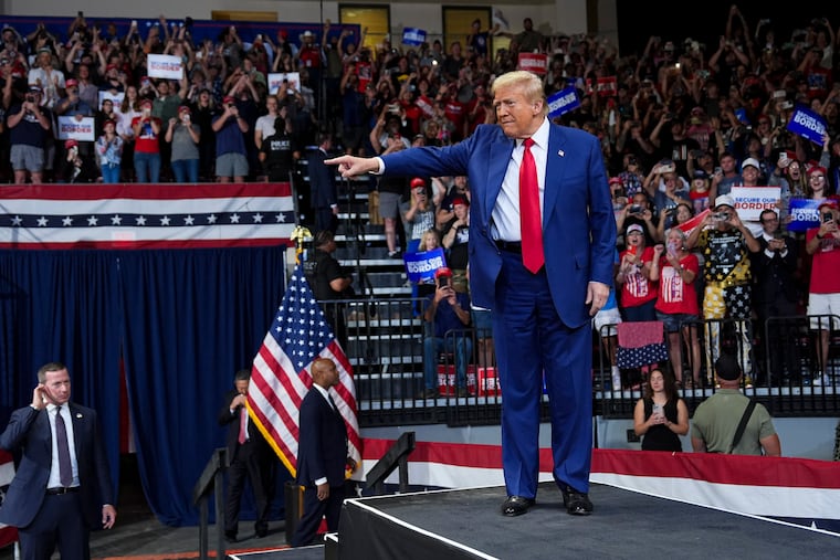 Former President Donald Trump greets the crowd at a campaign rally in Prescott, Ariz., in October 2024, as crowd members hold signs that say "secure our border." The former president has proposed mass deportation of undocumented individuals and increased use of tariffs on imports.