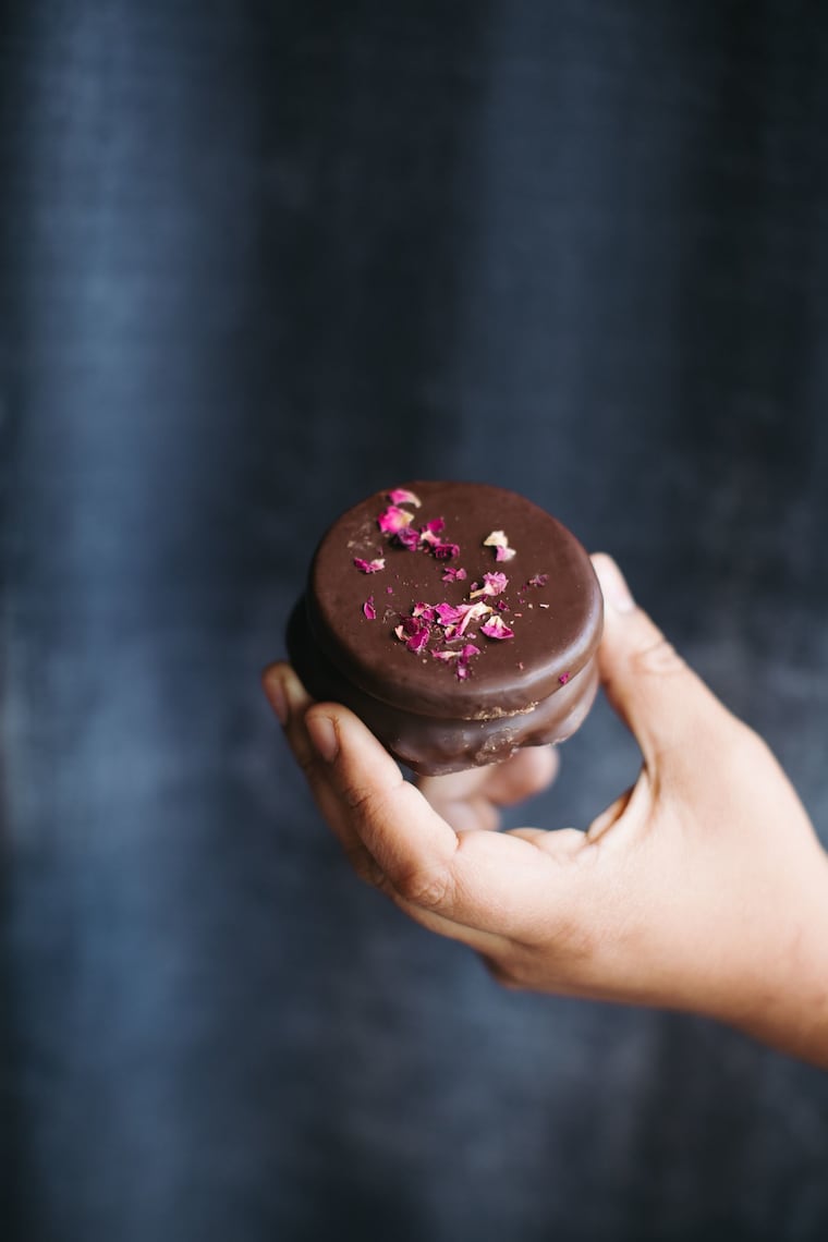 This alfajores is covered with chocolate and sprinkled with rose petals.